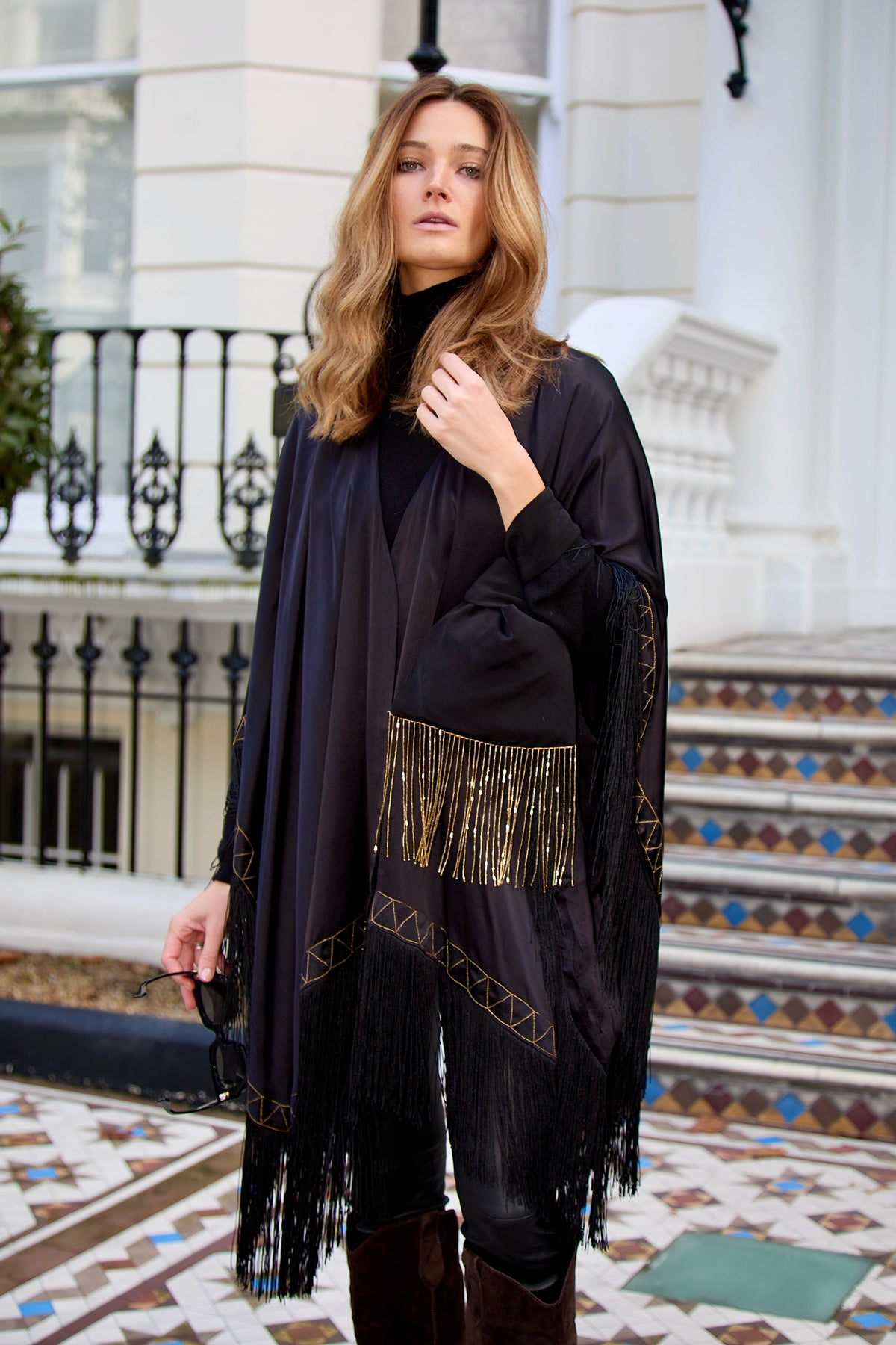 The Nomad Poncho in black silk with gold hand embroidery and black fringe, front view, London townhouse steps