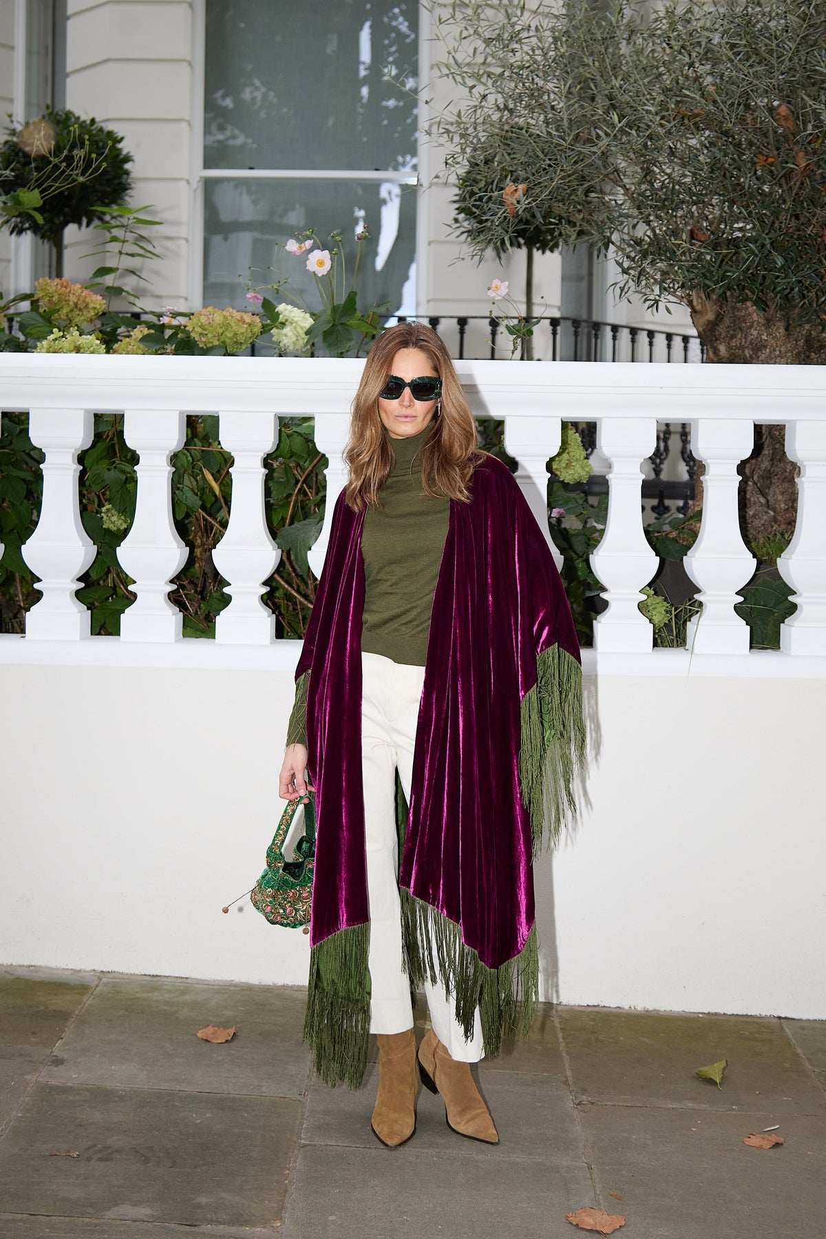 The Dahlia Poncho in magenta silk velvet with olive green fringe, worn open, London terrace