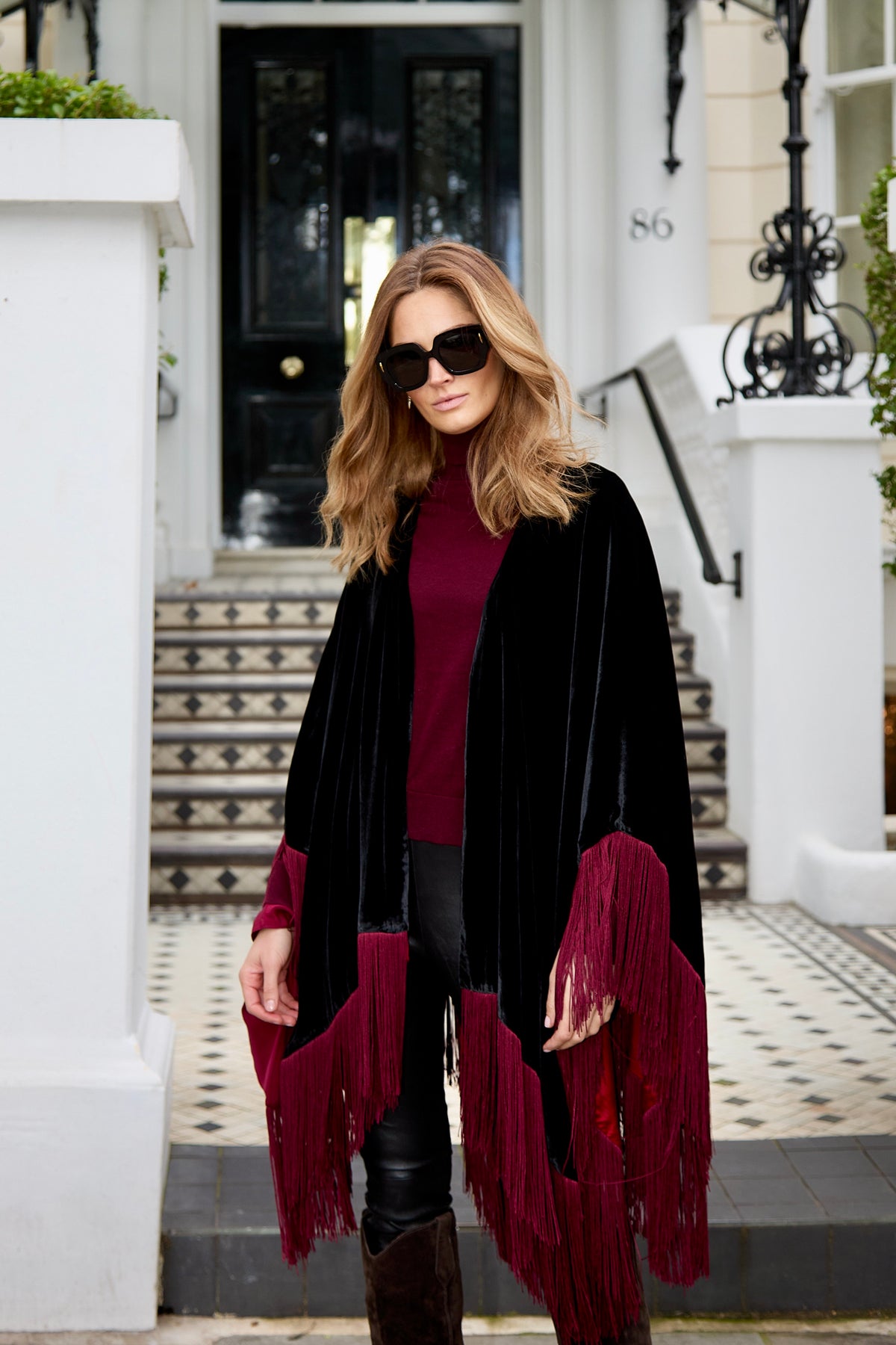 The Black Rose Poncho, short, in black silk velvet with dark red fringe, front view, London townhouse steps
