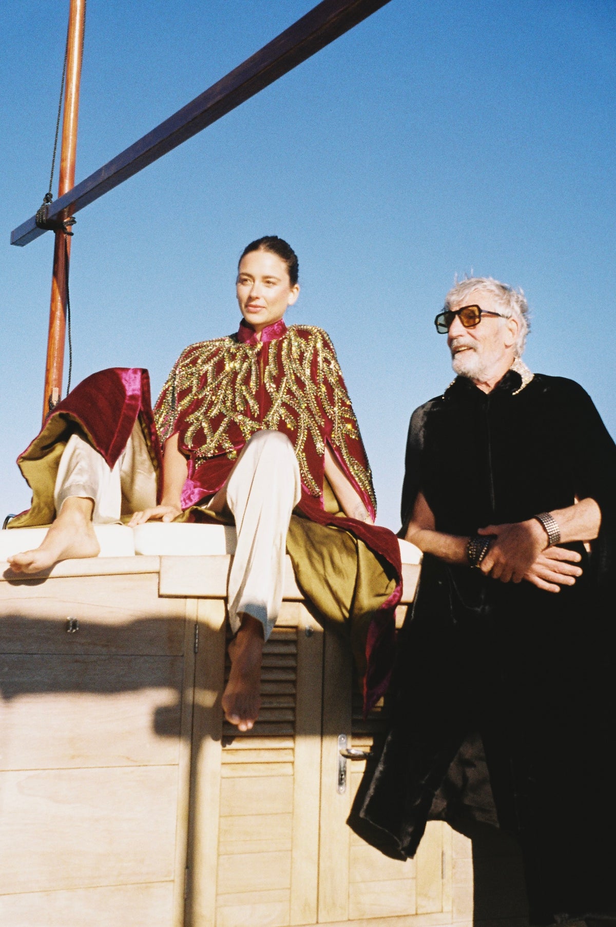 The Golden Collar Cape in black silk velvet with golden sequin collar, with the Royal Garden Cape, on a boat at sea