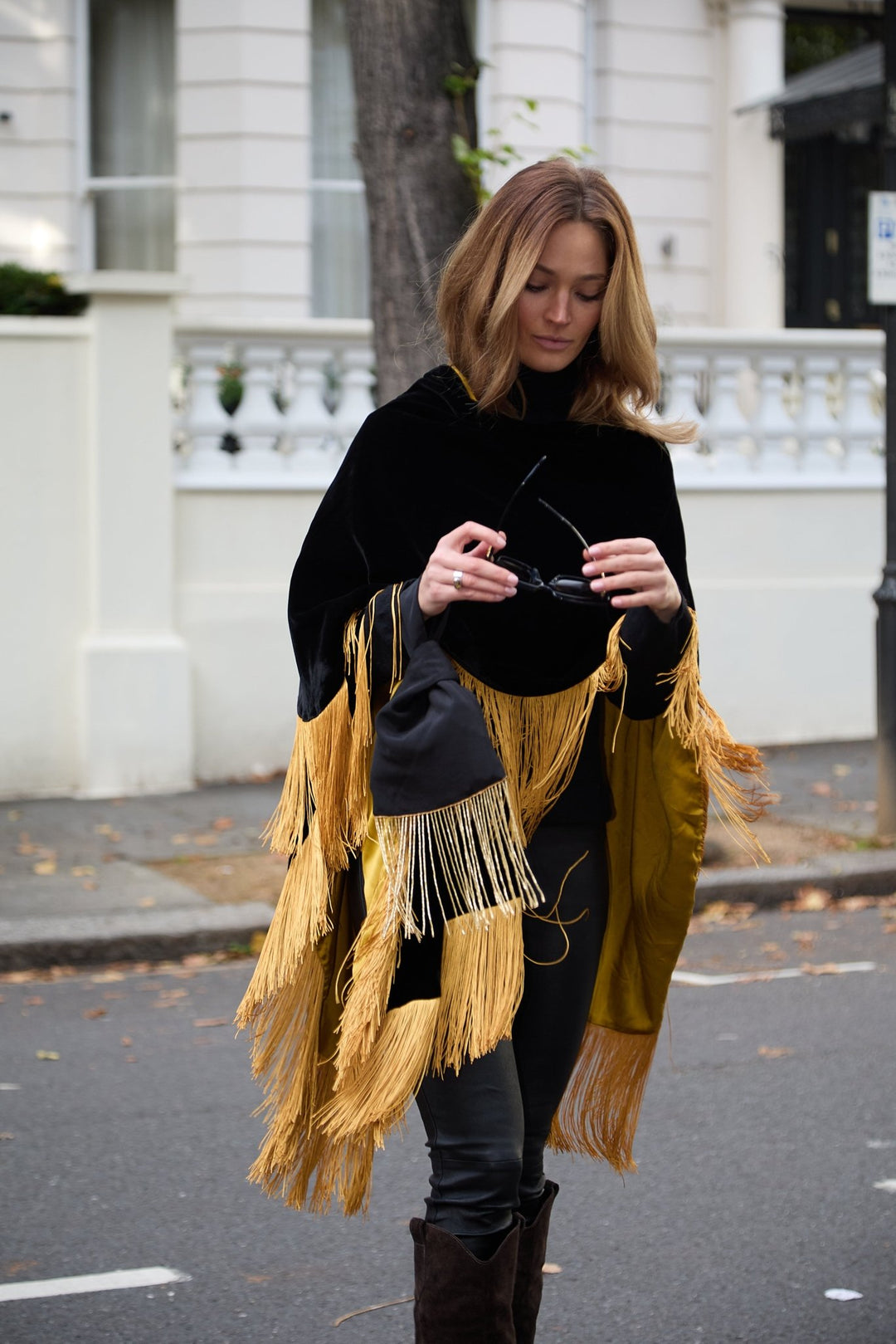 The Black Beaded Gold Knot Bag in black with gold beaded fringe, carried with the Golden Age Poncho, London street