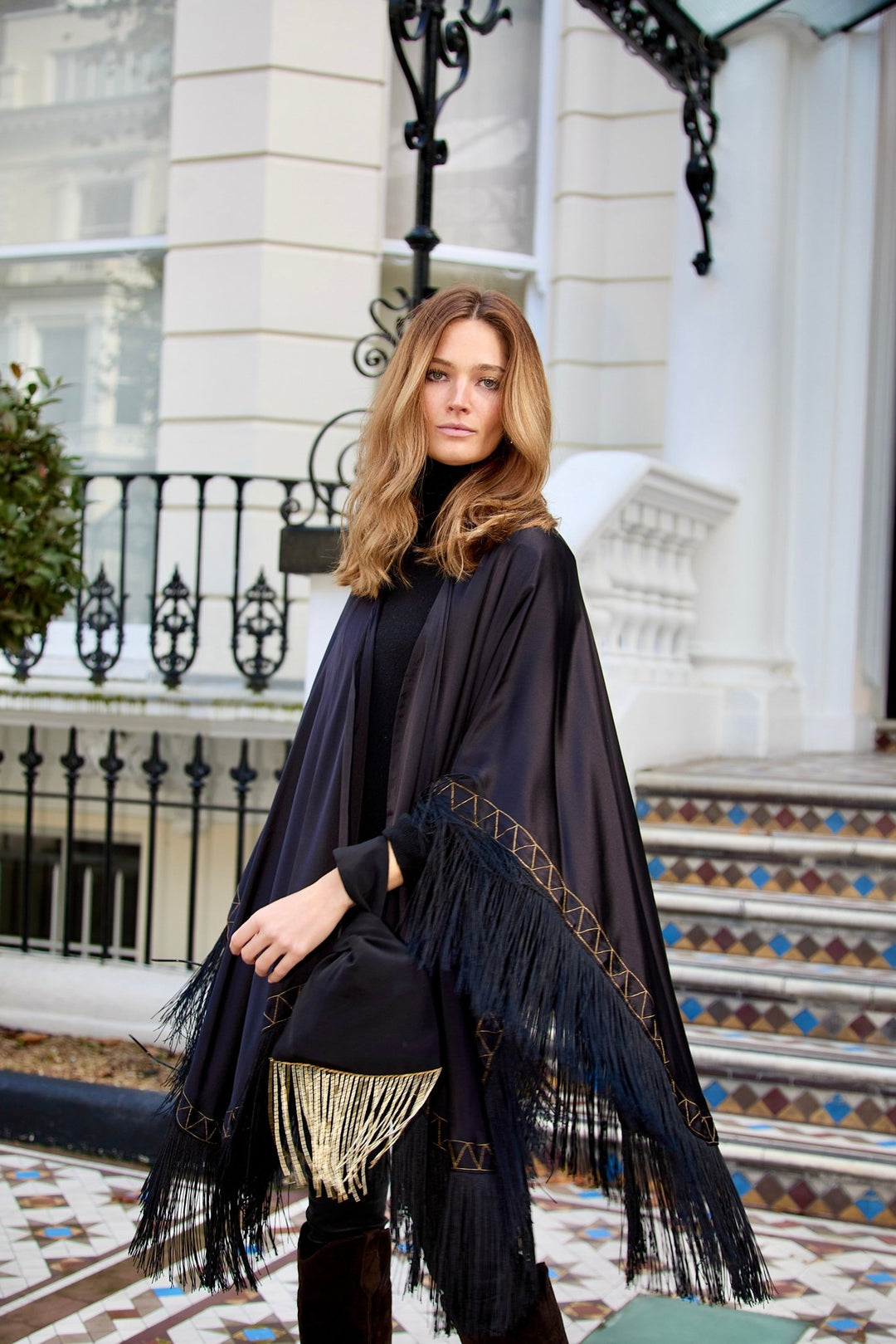 The Black Beaded Gold Knot Bag in black with gold beaded fringe, carried with the Nomad Poncho, London townhouse
