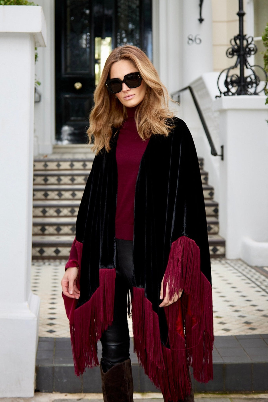 The Black Rose Poncho in black silk velvet with red fringe, front view, London townhouse steps