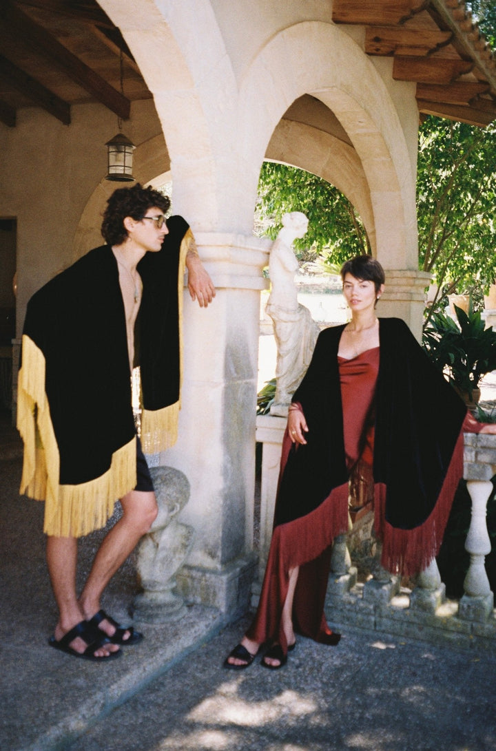 The Black Rose Poncho in black silk velvet with red fringe, garden archway