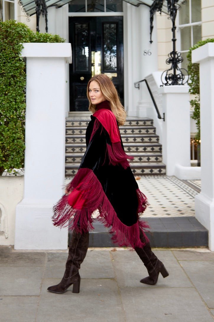 The Black Rose Poncho in black silk velvet with red fringe, walking, London townhouse steps
