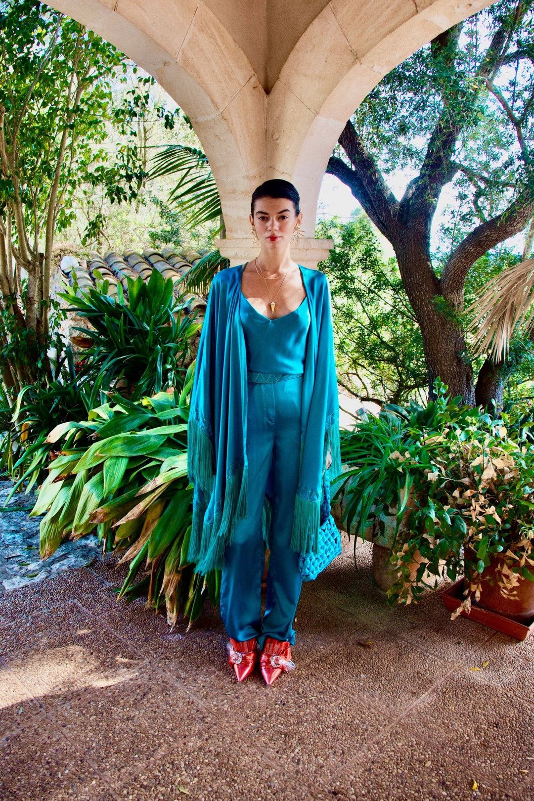 The Blue Poppy Camisole in turquoise silk, styled with the Blue Poppy Poncho, garden archway
