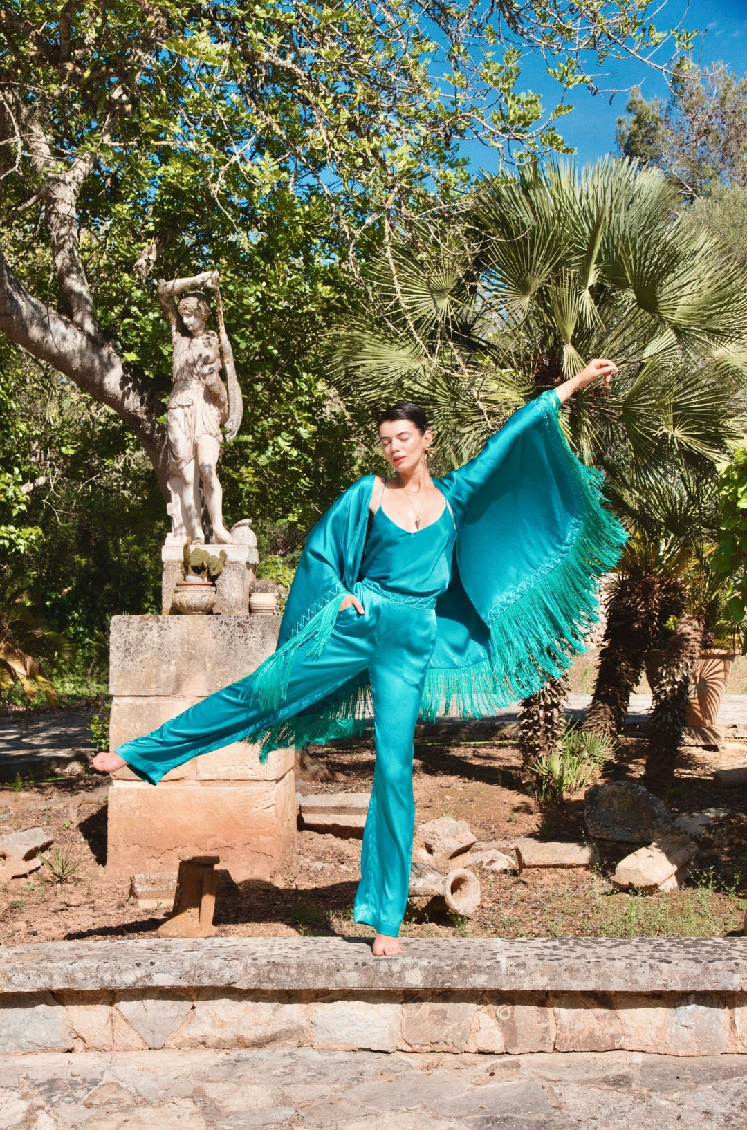 The Blue Poppy Poncho in turquoise silk with hand-embroidered border and fringe, with matching trousers, garden