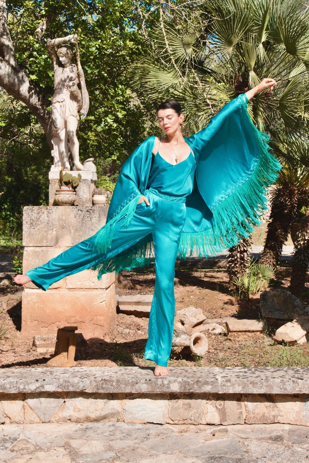 The Blue Poppy Trousers in turquoise silk, styled with the Blue Poppy Poncho, garden