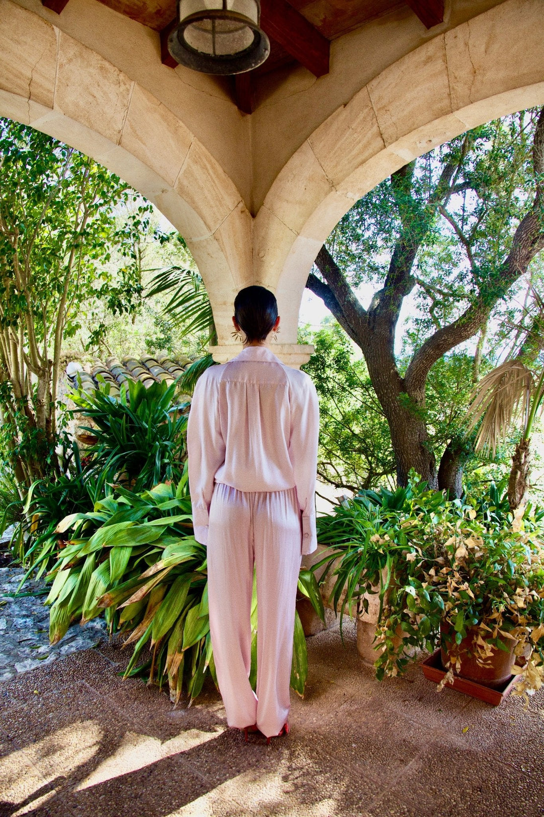 The Bow Blouse in pale pink silk twill, back view, garden archway