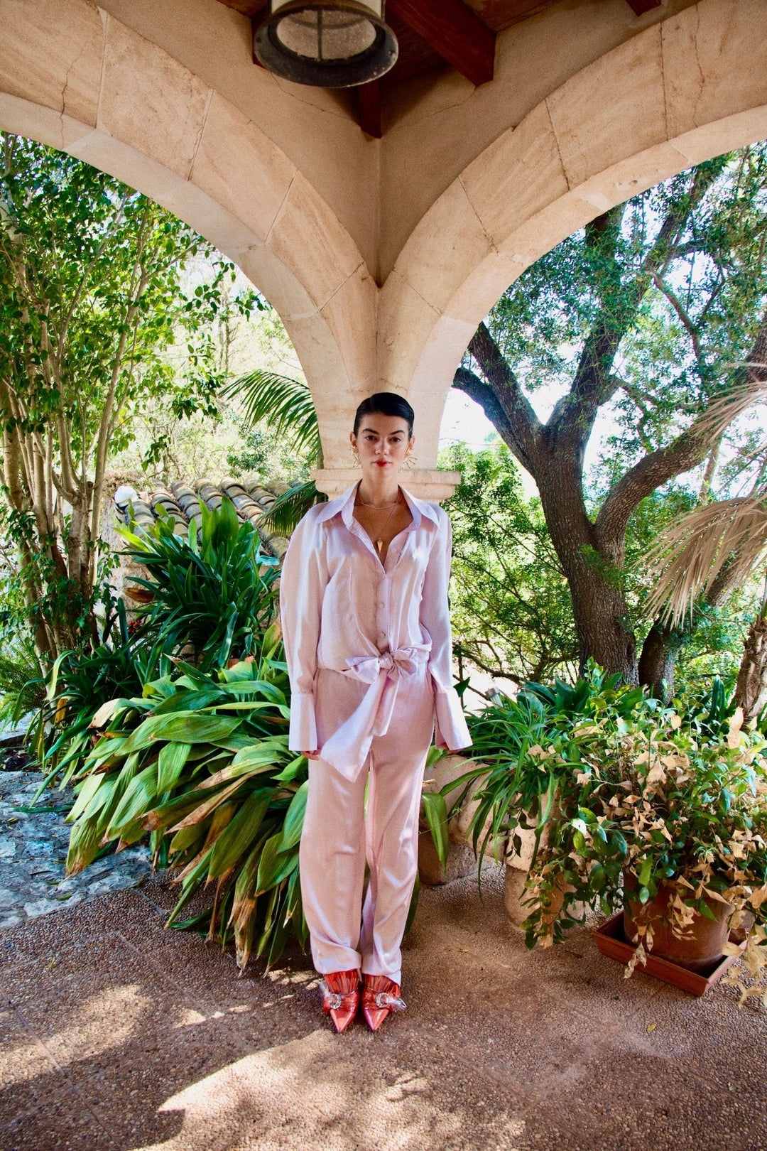 The Bow Blouse in pale pink silk twill, front view, garden archway