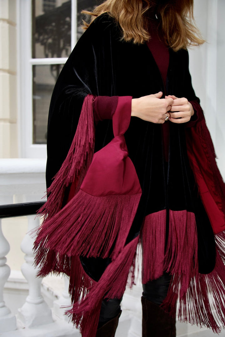 The Burgundy Knot Bag in burgundy silk velvet with long fringe, carried with a black velvet poncho, London townhouse