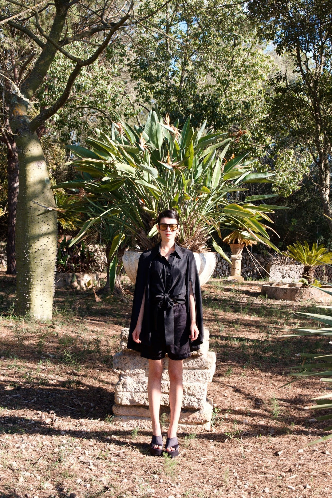 The Cape Sleeve Blouse in black silk twill, front view, garden