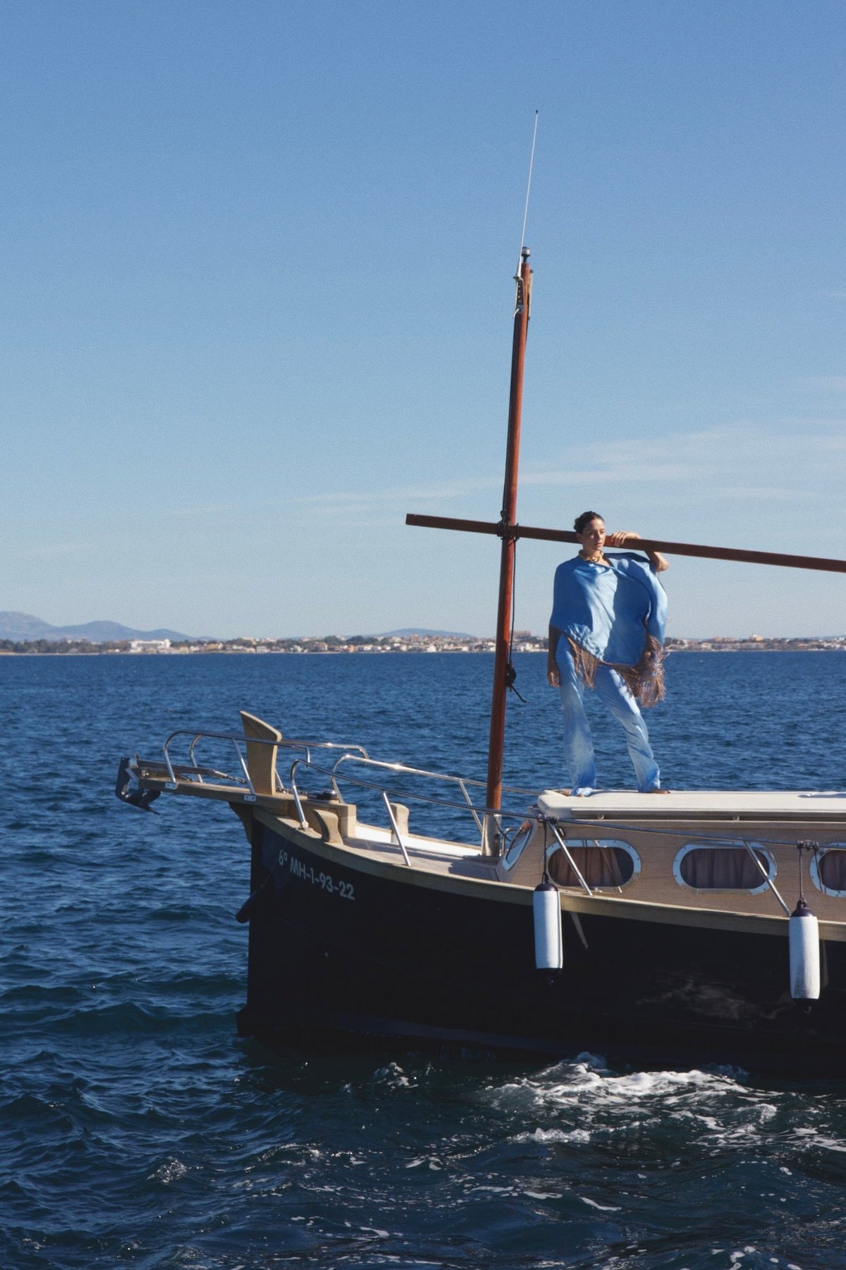 The Cornflower Poncho in powder blue silk with fringed hem, on a sailing boat at sea