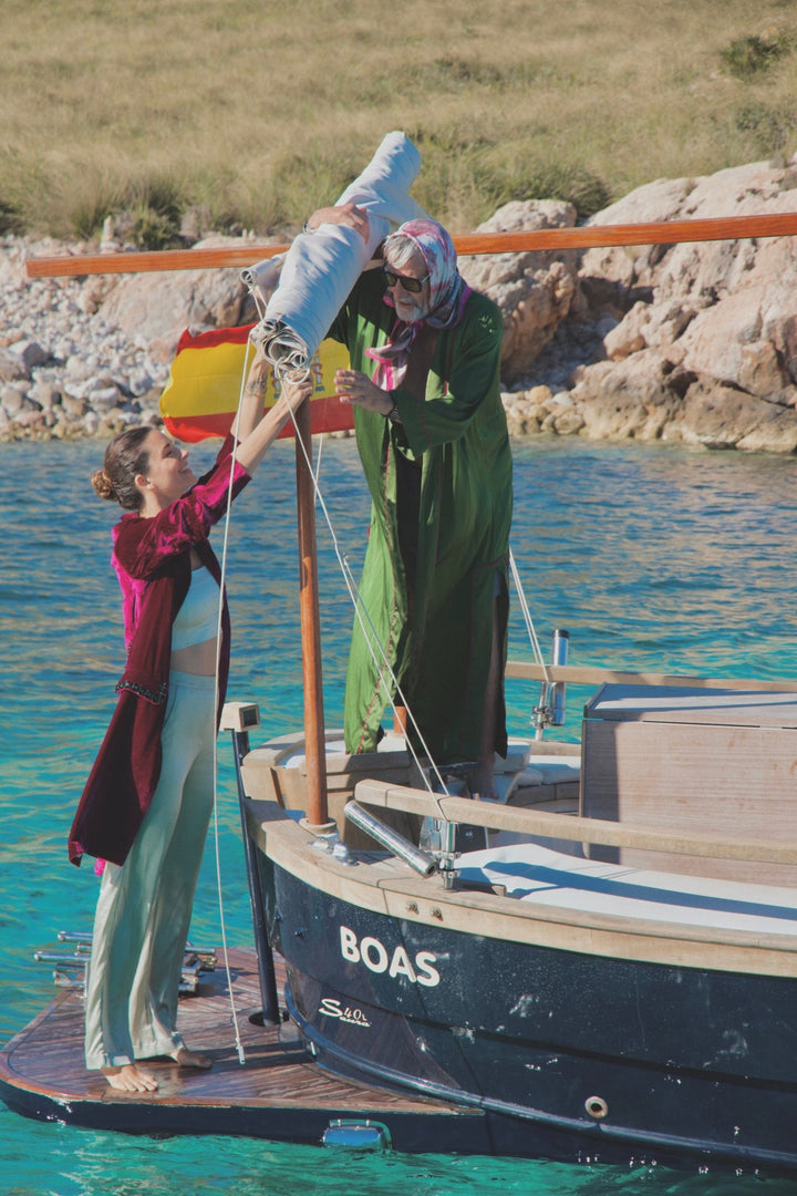 The Dahlia Coat in magenta silk velvet with embroidered trim, on a sailing boat
