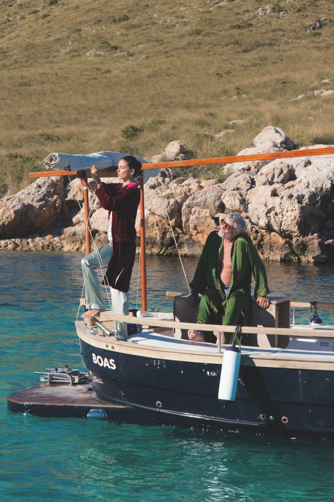The Dahlia Coat in magenta silk velvet with embroidered trim, on a sailing boat