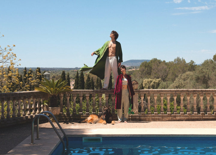 The Dahlia Coat in magenta silk velvet with embroidered trim, stone terrace by a pool