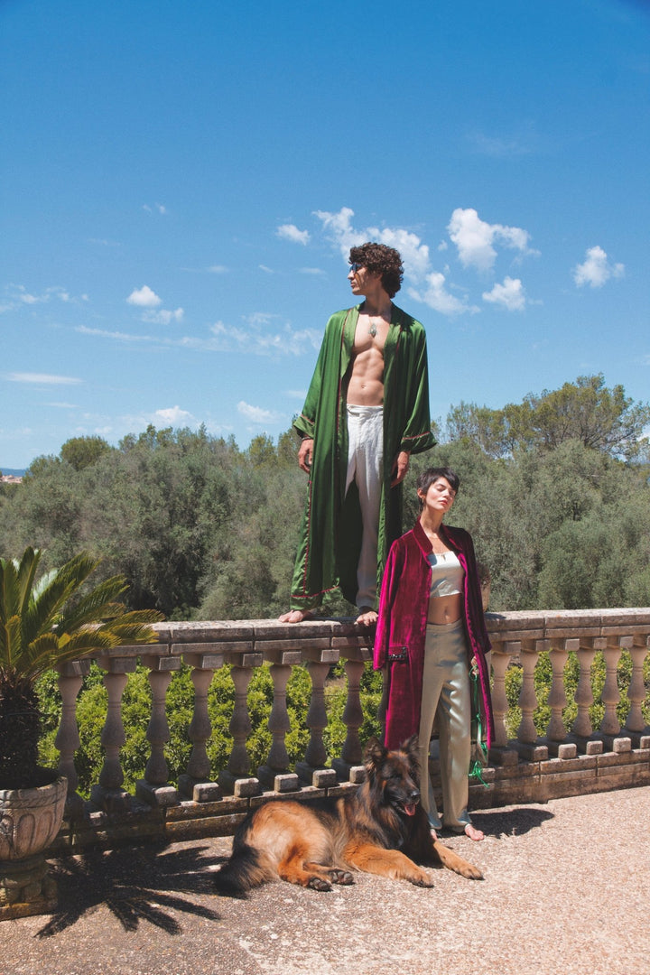 The Dahlia Coat in magenta silk velvet with embroidered trim, stone terrace with a dog