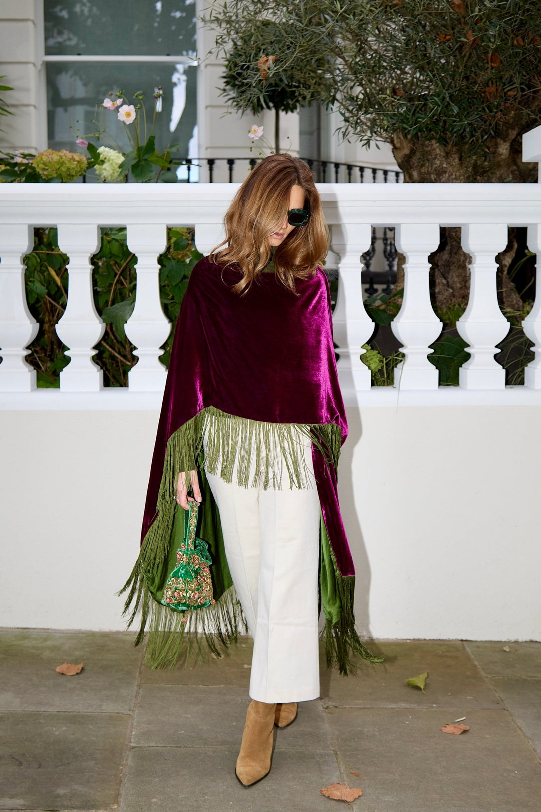 The Dahlia Poncho in magenta silk velvet with olive green fringe, front view, London terrace