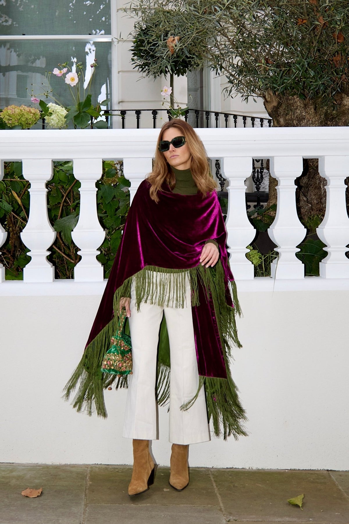 The Dahlia Poncho in magenta silk velvet with olive green fringe, front view, London terrace