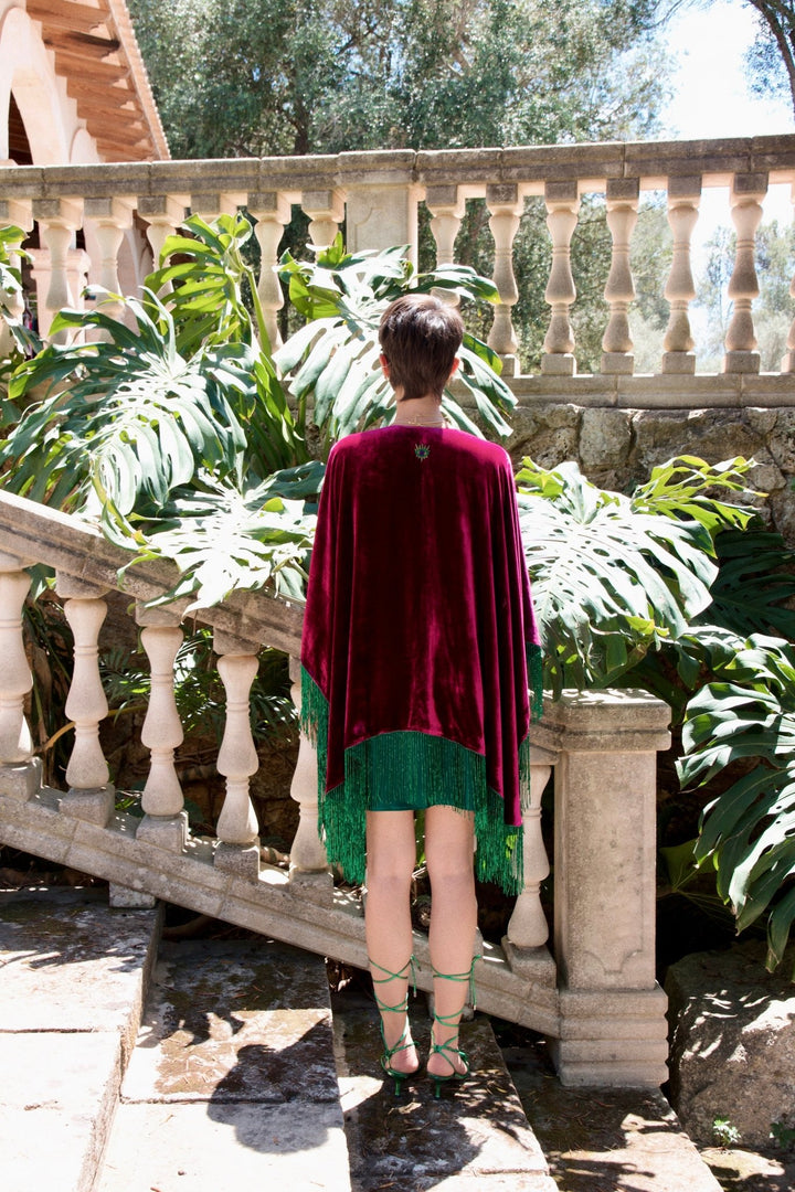 The Dahlia Sparkle Poncho in magenta silk velvet with emerald beaded fringe, back view, stone staircase