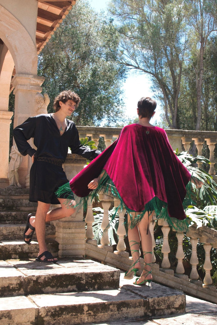 The Dahlia Sparkle Poncho in magenta silk velvet with emerald beaded fringe, in motion, stone staircase