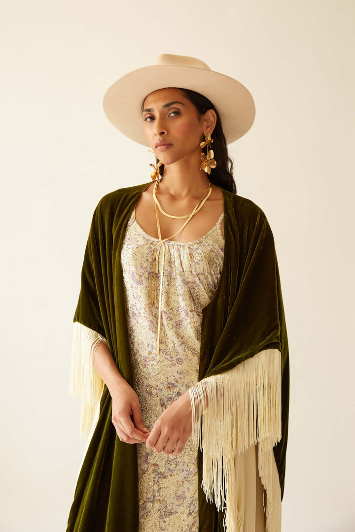 The Evergreen Poncho in olive green silk velvet with cream fringe, close-up styled with a hat, studio