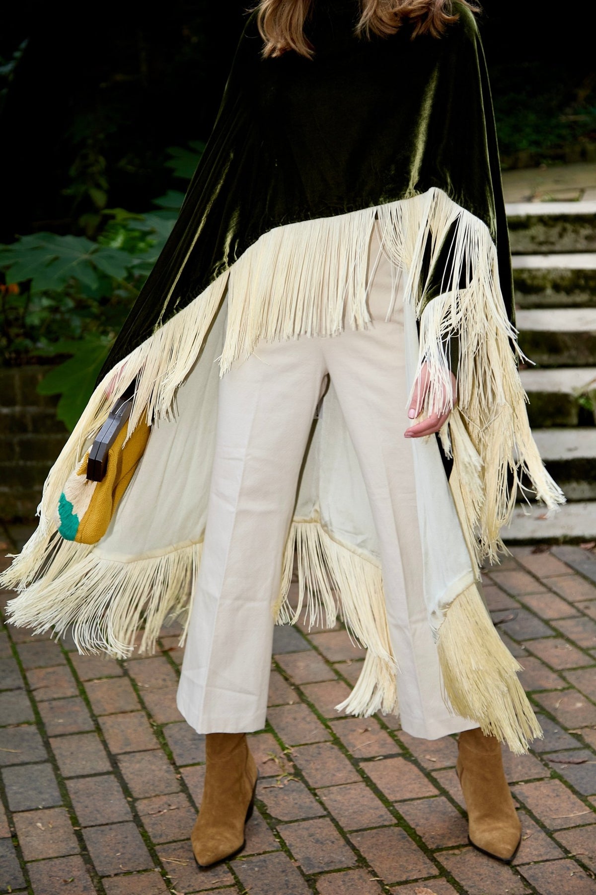 The Evergreen Poncho in olive green silk velvet with cream fringe, fringe detail, London street
