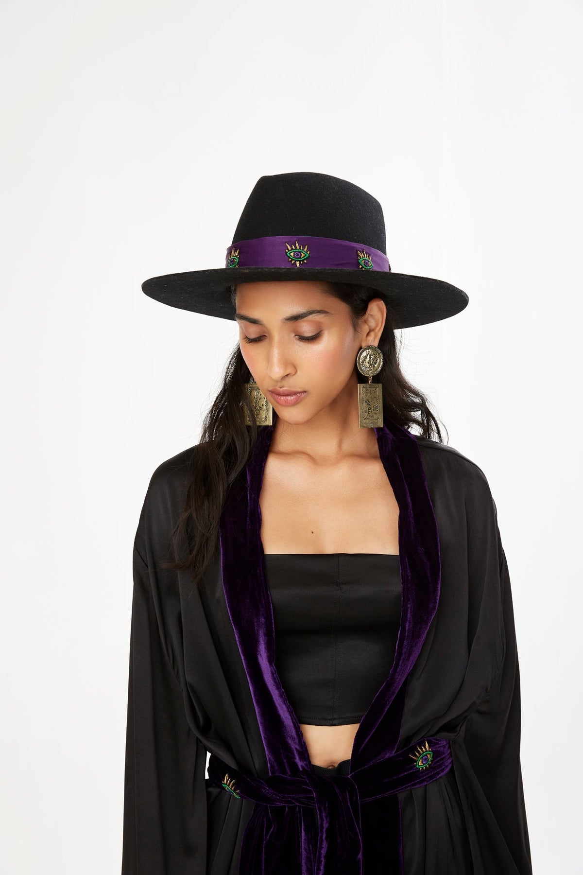 The Eyecatcher Hatband in purple silk with embroidered eyes and green fringe, on a black hat, front view, studio