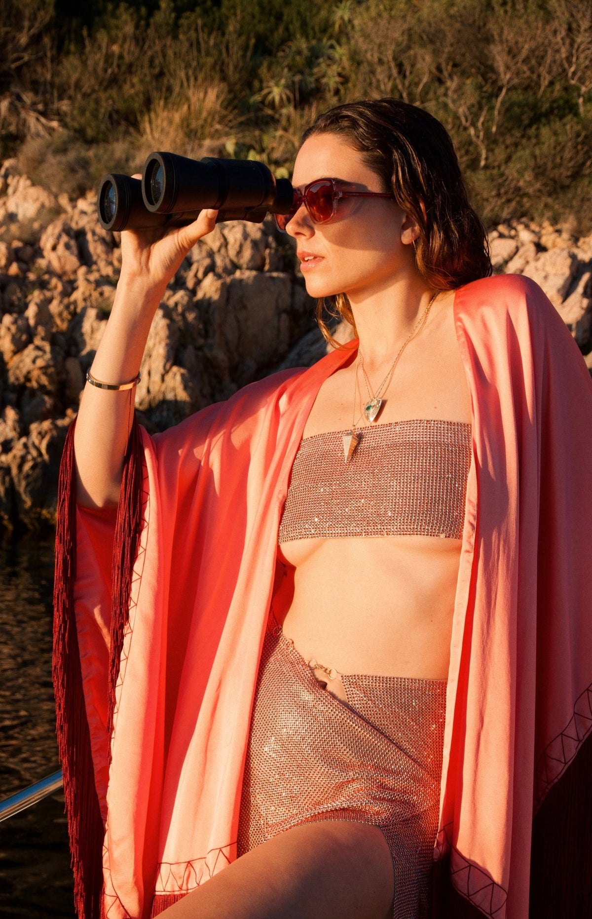 The Fire Bolt Poncho in coral silk with red fringe, close-up, on a sailing boat