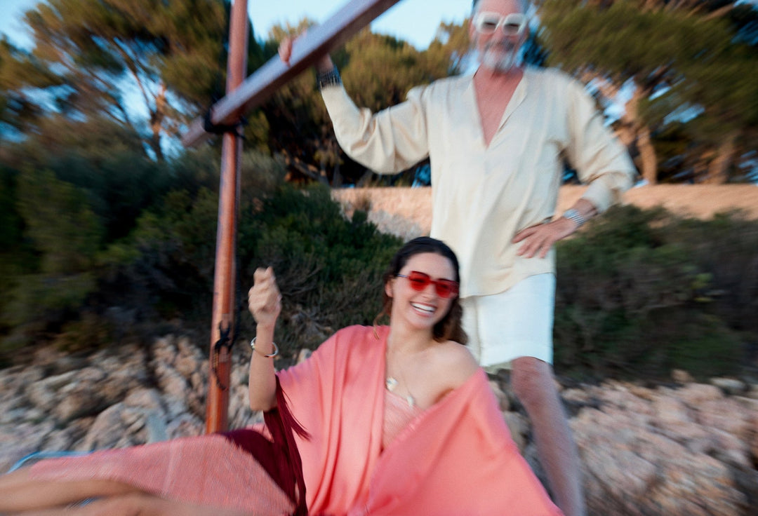 The Fire Bolt Poncho in coral silk with red fringe, on a sailing boat