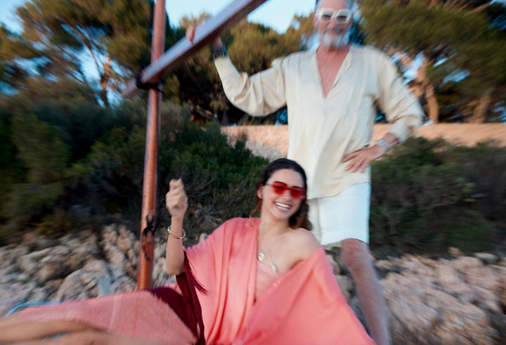 The Fire Bolt Poncho in coral silk with red fringe, on a sailing boat