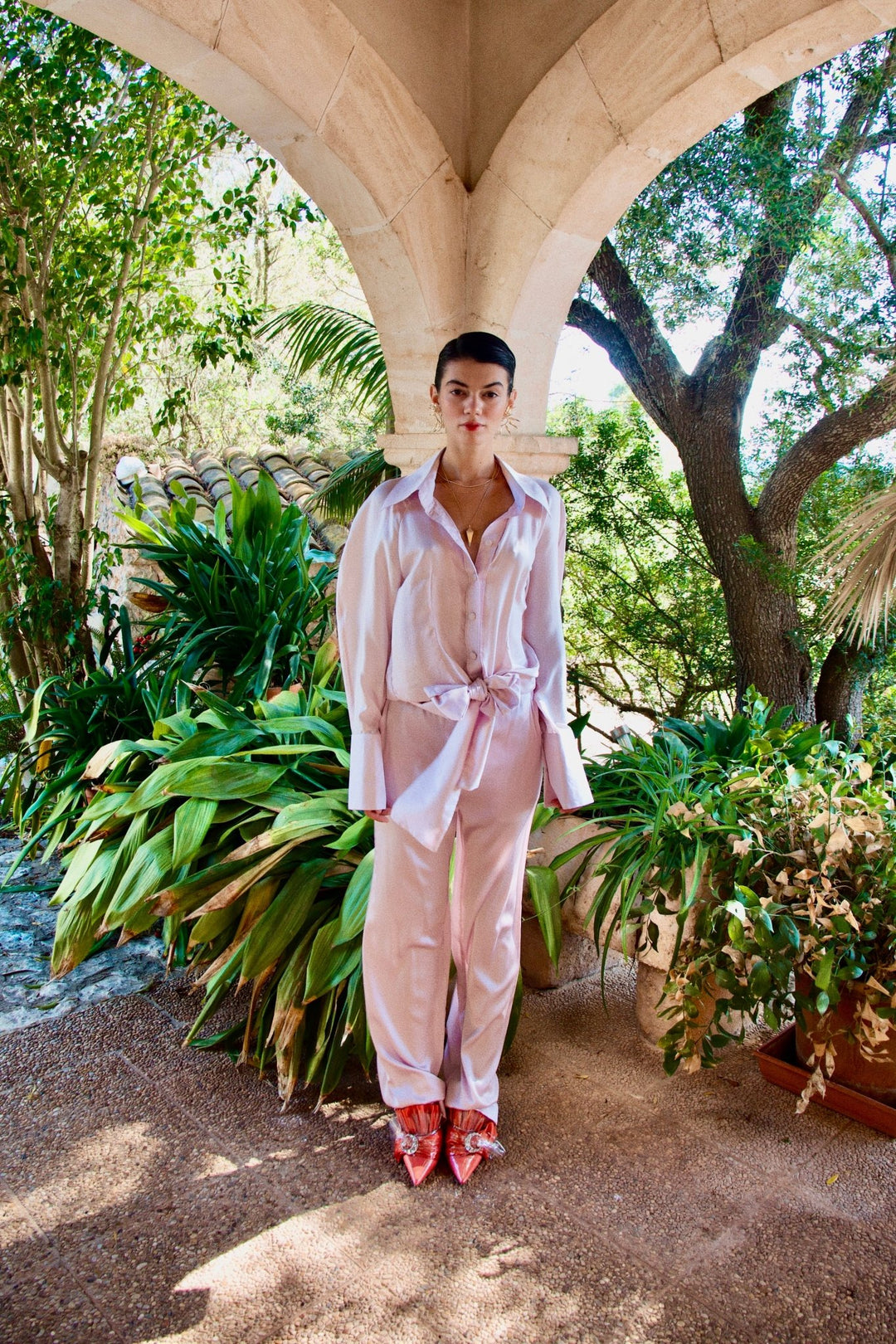 The Fondant Pink Trousers in pale pink silk, styled with the Bow Blouse, front view, garden archway