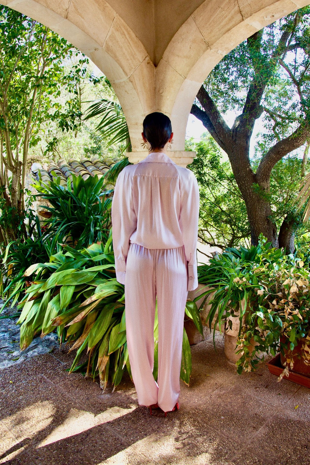 The Fondant Pink Trousers in pale pink silk, styled with the Bow Blouse, back view, garden archway