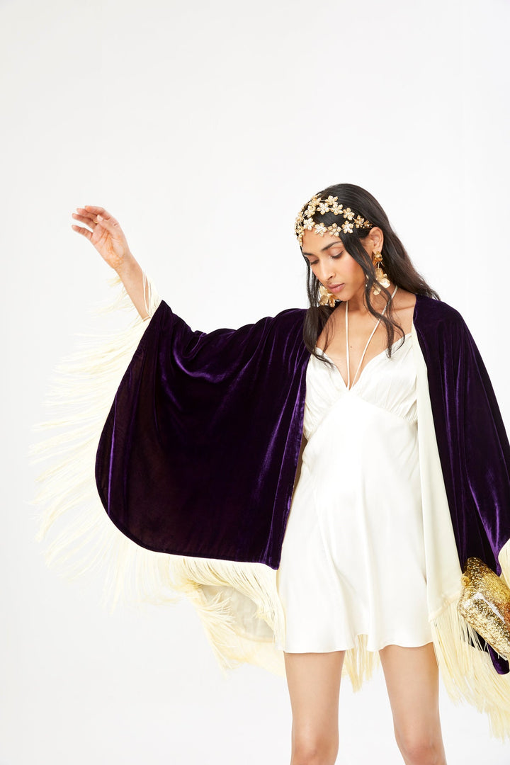 The Gatsby Poncho in purple silk velvet with champagne fringe, styled over a cream slip dress, studio