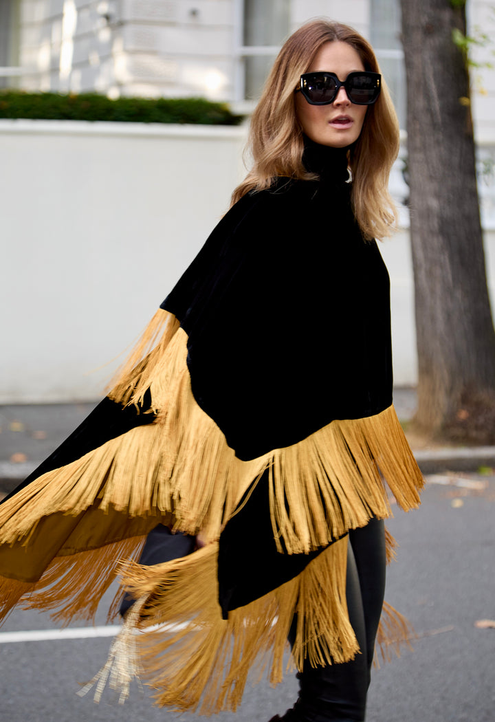 The Golden Age Poncho in black silk velvet with gold fringe, front view, London street