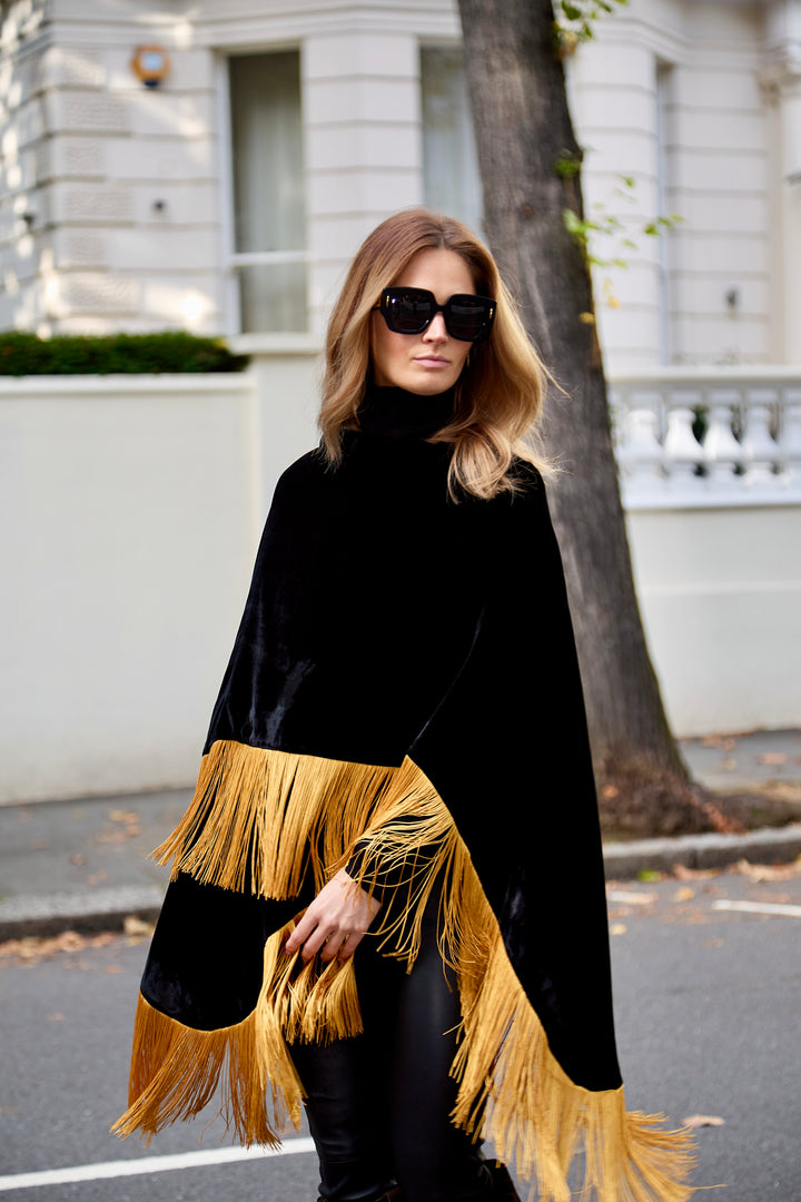 The Golden Age Poncho in black silk velvet with gold fringe, front view, London street