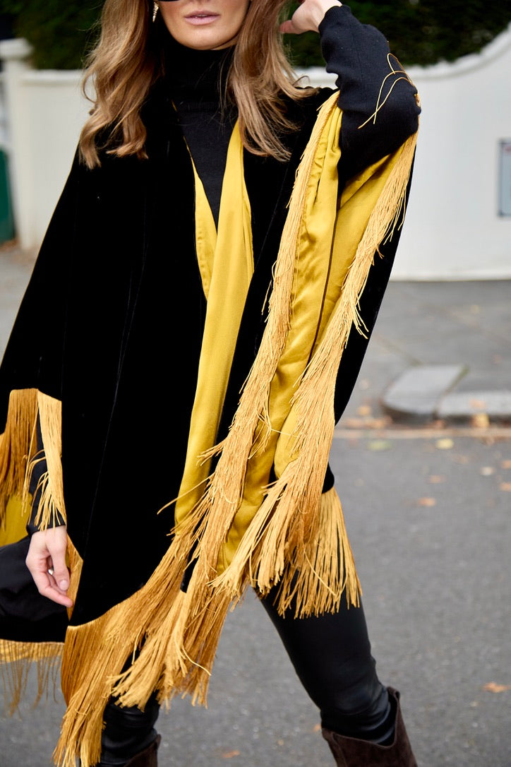 The Golden Age Poncho in black silk velvet with gold fringe, gold lining detail, London street