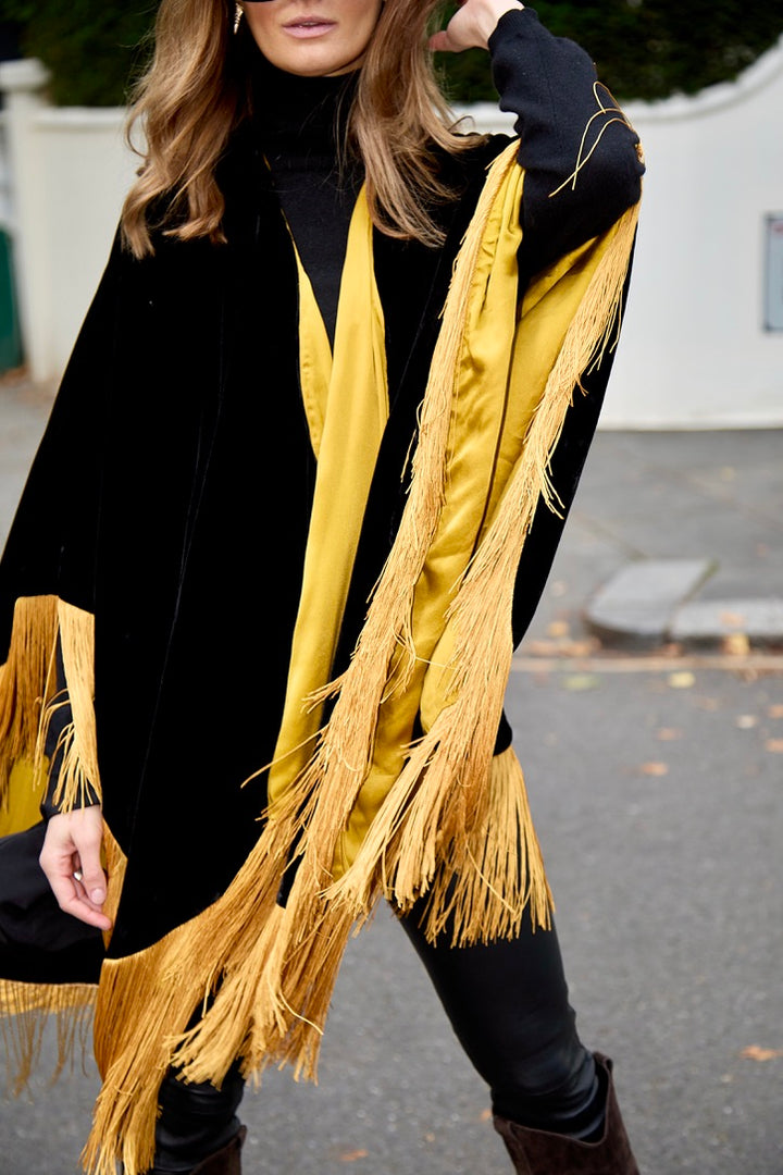 The Golden Age Poncho in black silk velvet with gold fringe, gold lining detail, London street