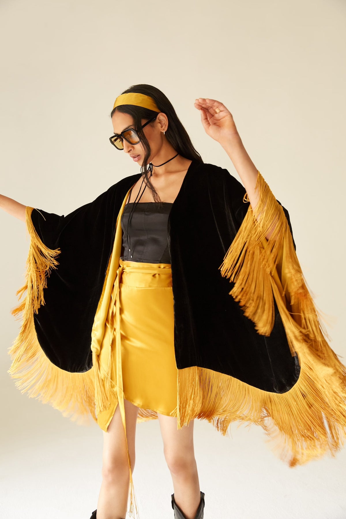 The Golden Age Poncho in black silk velvet with gold fringe, styled with a gold skirt, studio