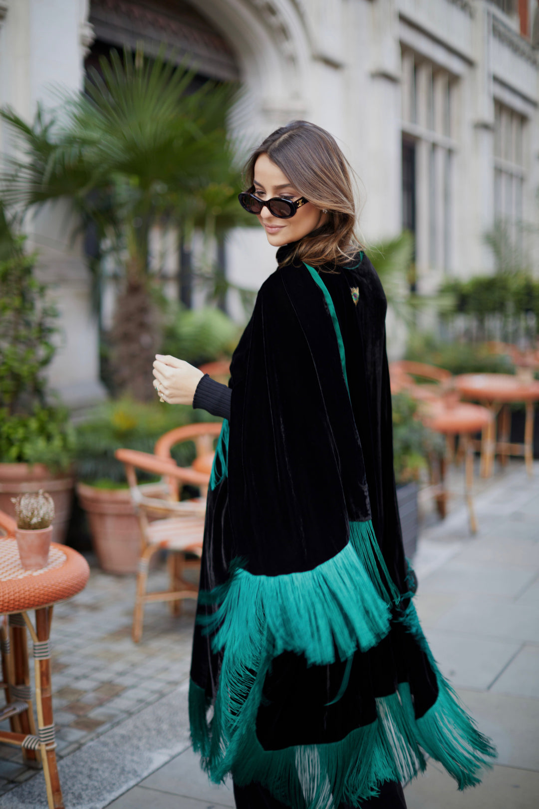 The Gypset Poncho in black silk velvet with emerald fringe, back view, London street