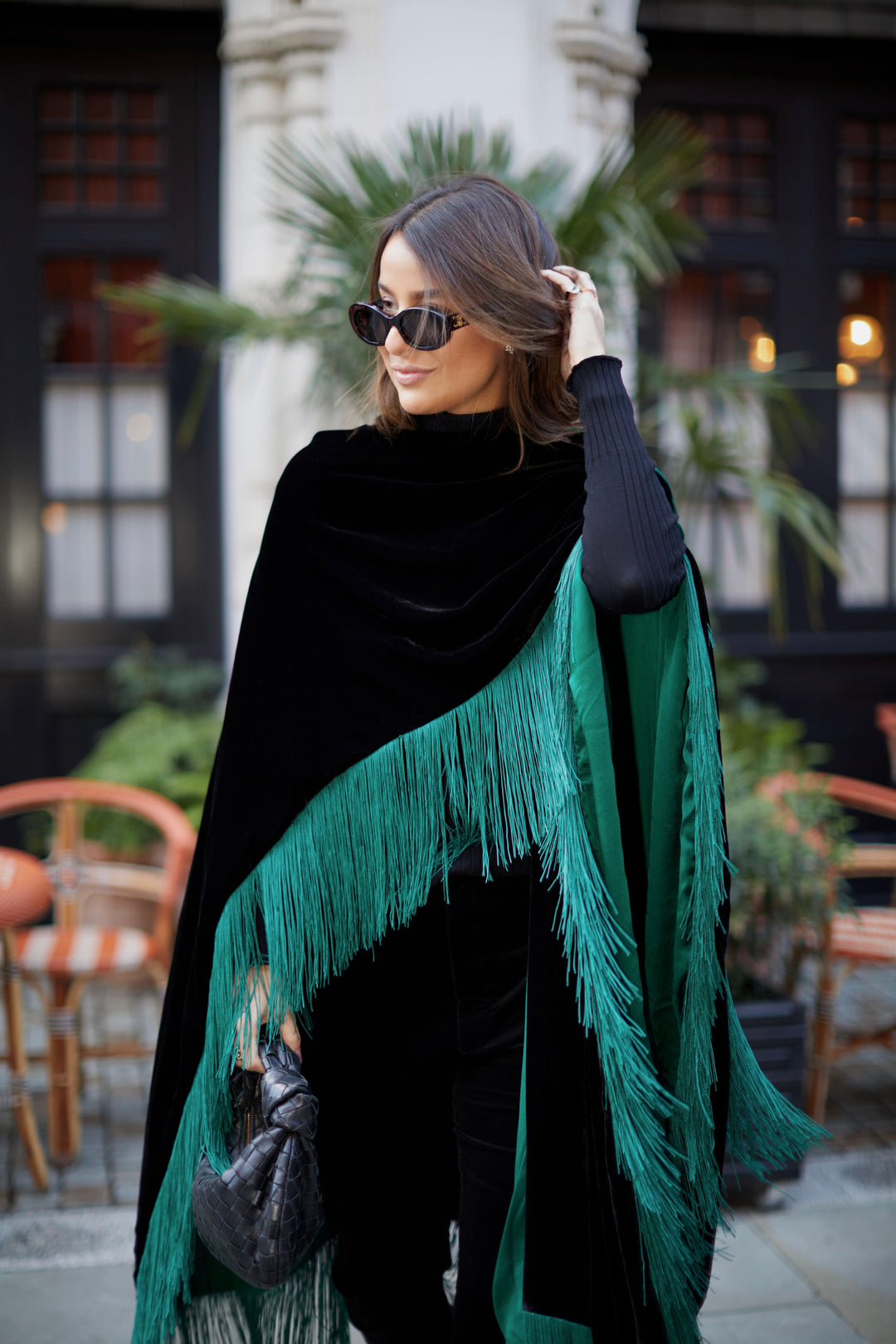 The Gypset Poncho in black silk velvet with emerald fringe, back view, London street