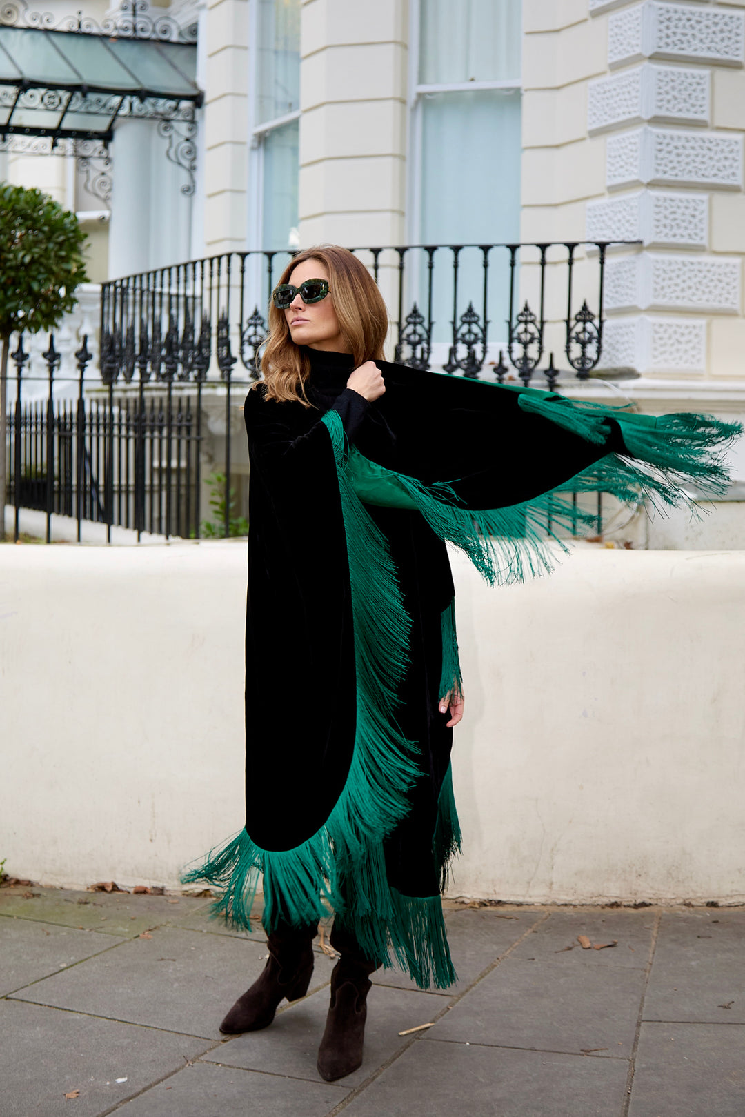 The Gypset Poncho in black silk velvet with emerald fringe, side view, London street