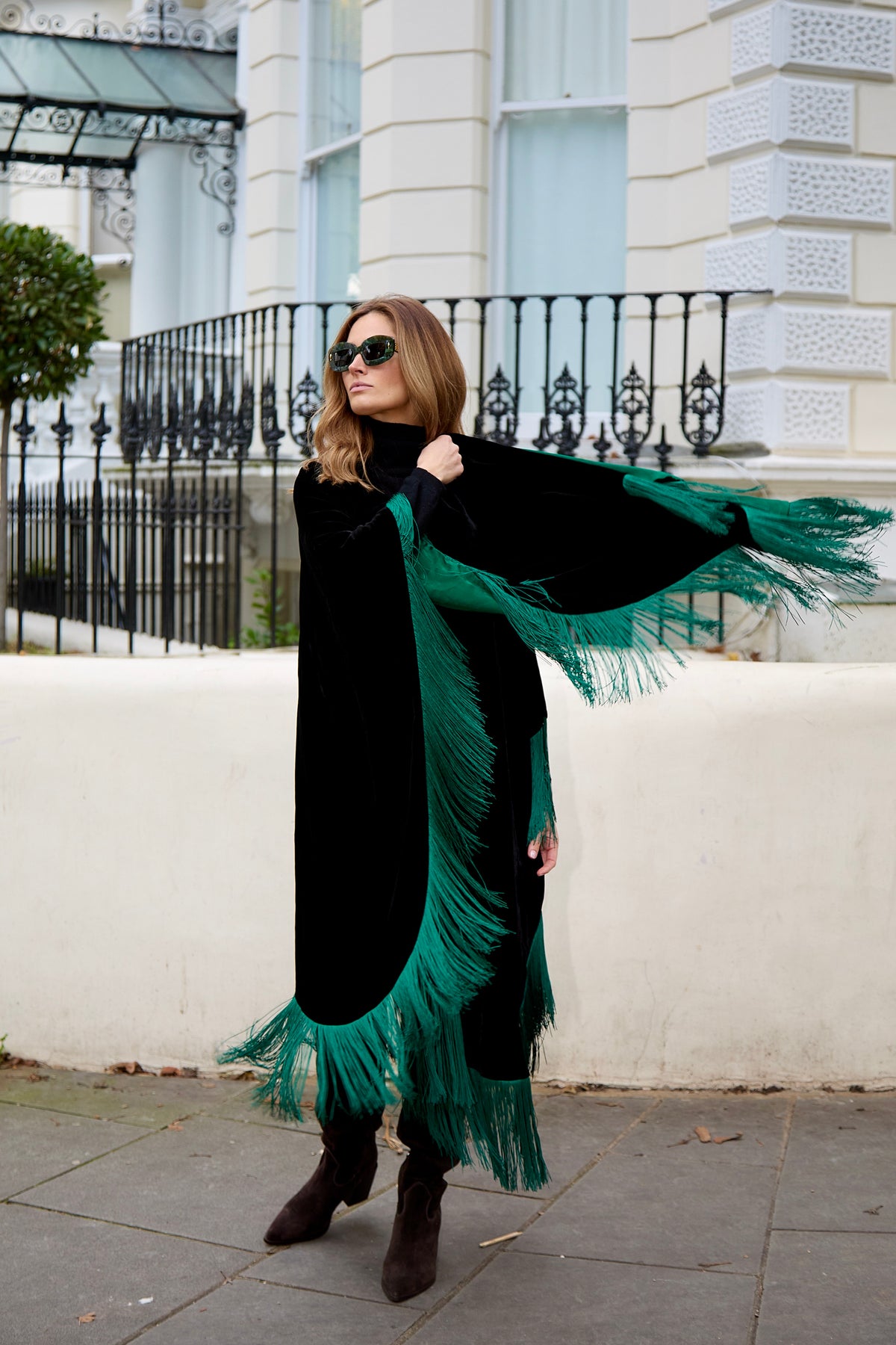 The Gypset Poncho in black silk velvet with emerald fringe, side view, London street