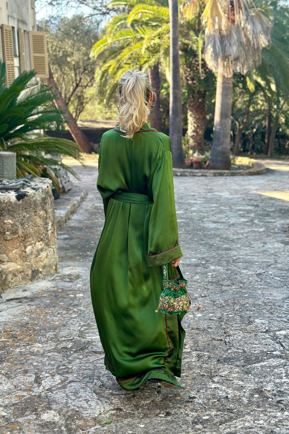 The Jade Vine Kimono in emerald green heavy silk, back view, garden courtyard