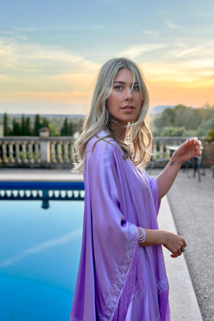 The Lavender Poncho in lavender silk with fringed hem, front view, terrace at sunset