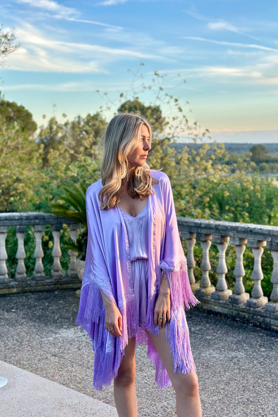 The Lavender Poncho in lavender silk with fringed hem, worn with the Lavender Playsuit, terrace at sunset
