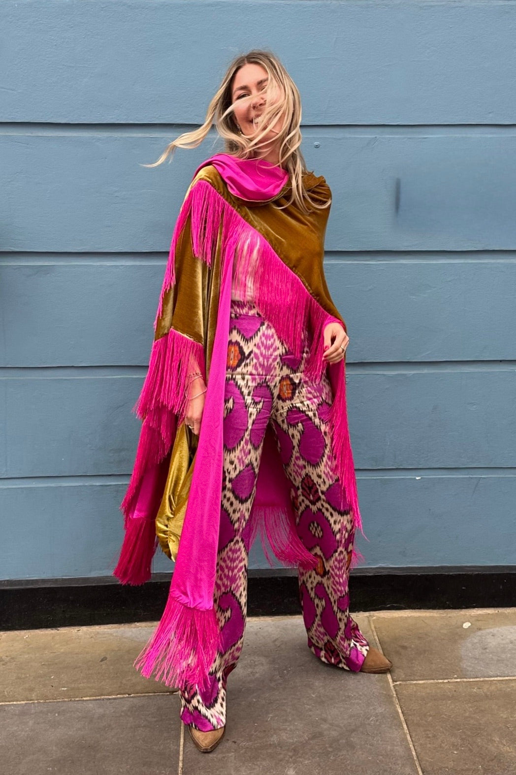 The Limoncello Poncho in golden yellow silk velvet with pink fringe, styled with printed trousers, outdoors