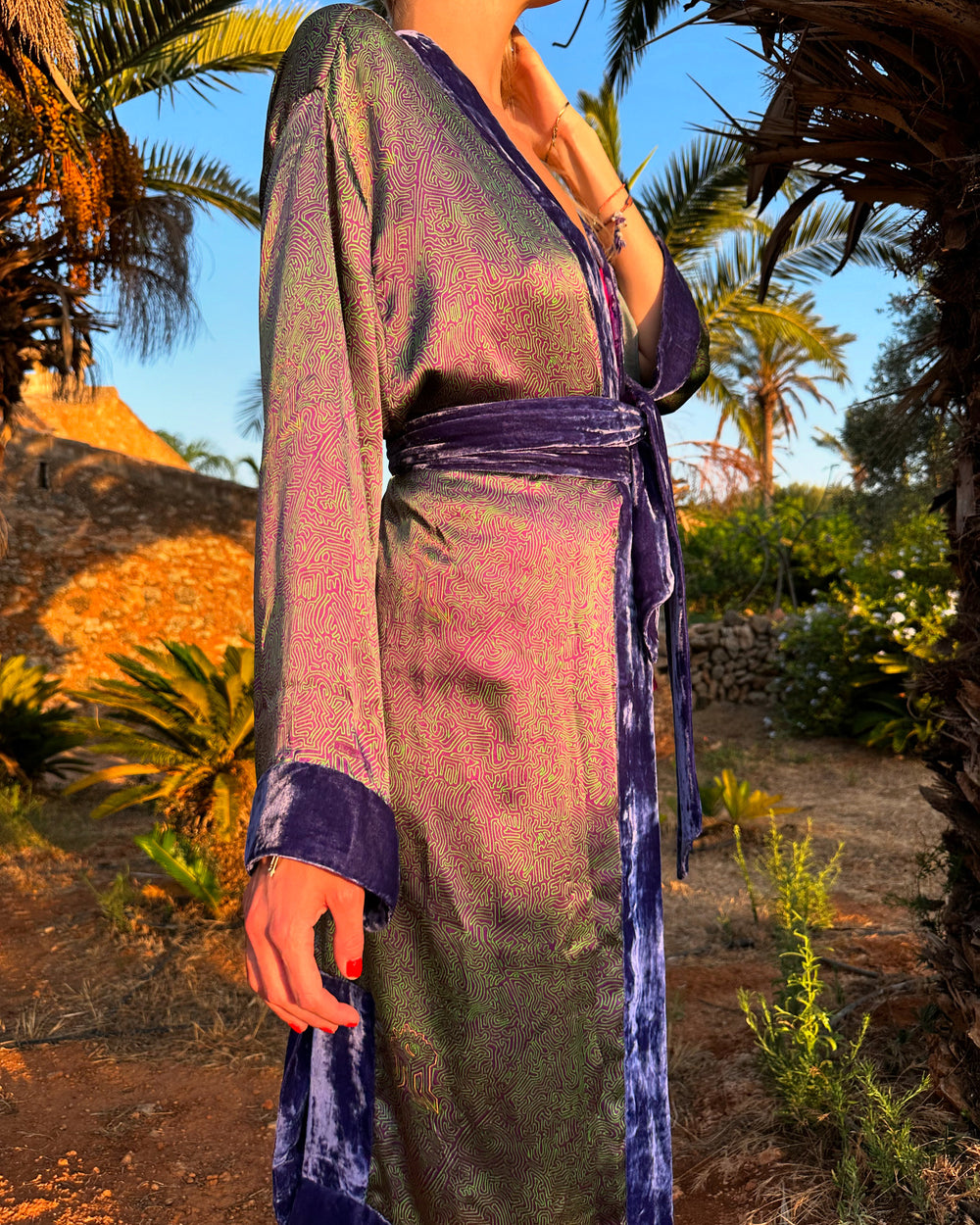 The Mazestroom Kimono, Purple and Green, in iridescent green and purple maze-print silk with velvet trim, belted detail, palm garden