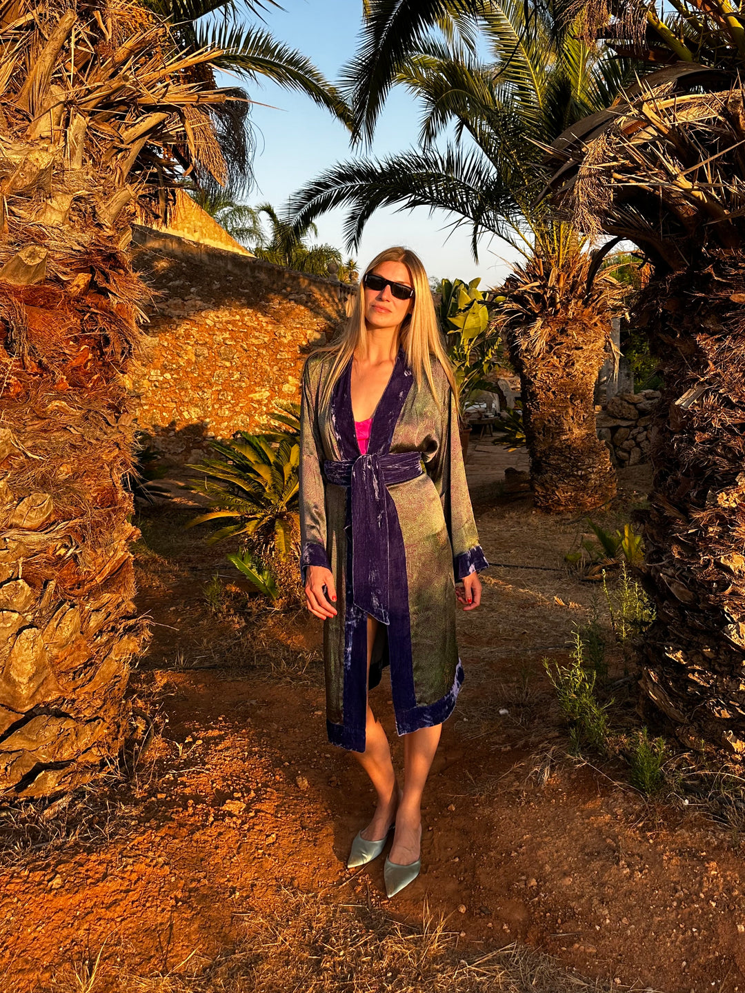 The Mazestroom Kimono, Purple and Green, in iridescent green and purple maze-print silk with velvet trim, front view, palm garden