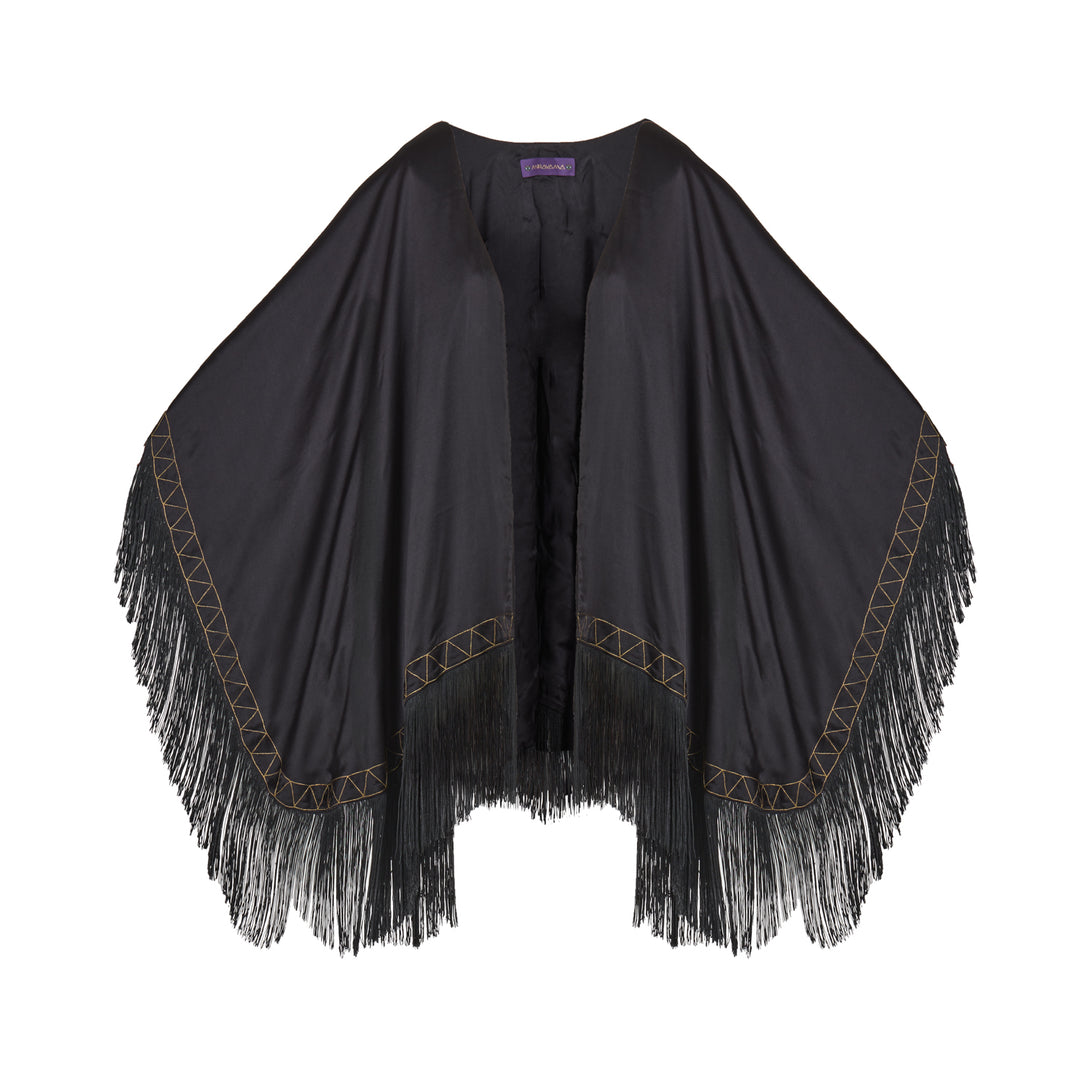The Nomad Poncho in black silk with gold hand embroidery and black fringe, flat lay, studio